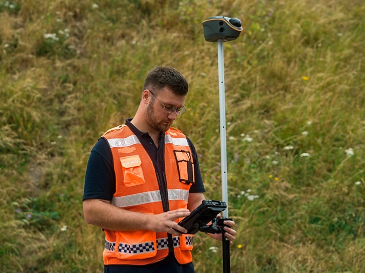Agrimensor que utiliza um rover GNSS RTK da CHC Navigation num poste de levantamento para recolher dados de posicionamento no terreno em terreno aberto
